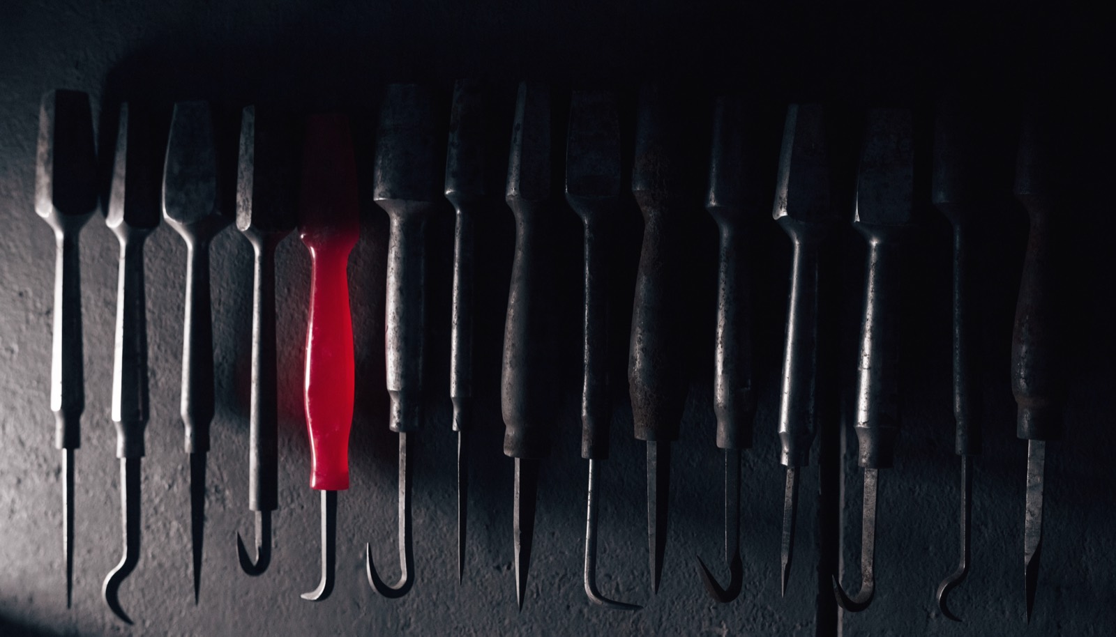 Hand tools hung in a precise row on a dark workshop wall, one of them with a crimson handle.